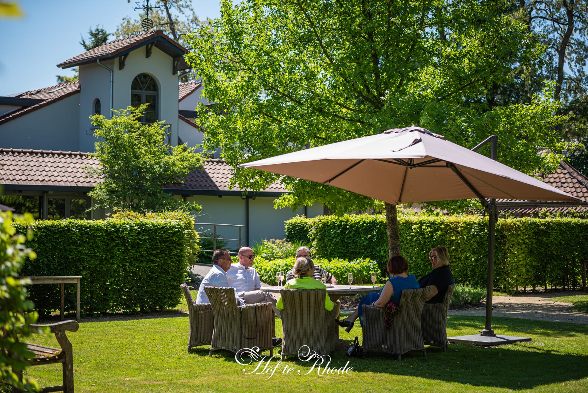 Gasten aan tafel in de tuin onder een parasol